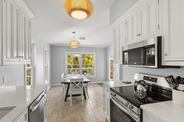 kitchen with appliances with stainless steel finishes, wood tiled floor, pendant lighting, and white cabinets