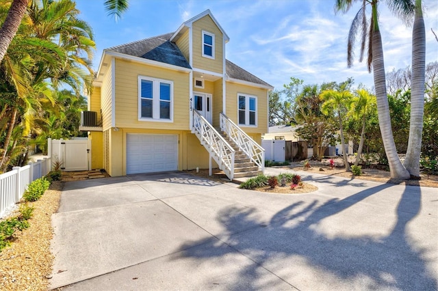 raised beach house with concrete driveway, fence, a garage, cooling unit, and stairs