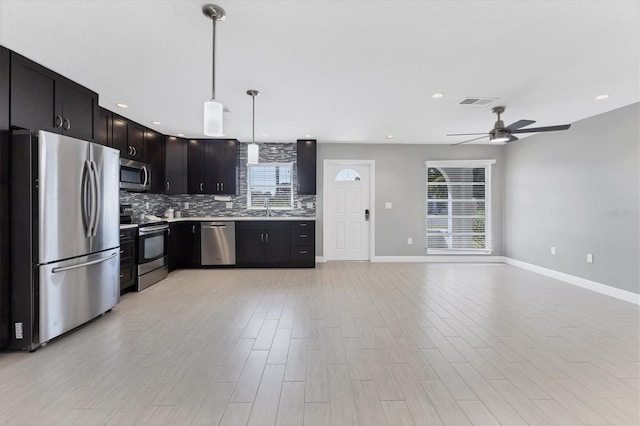kitchen featuring sink, decorative backsplash, hanging light fixtures, stainless steel appliances, and light hardwood / wood-style flooring