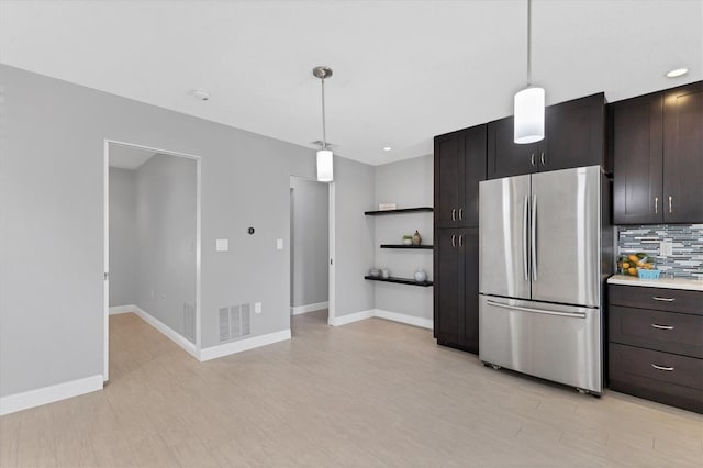 kitchen featuring stainless steel refrigerator, tasteful backsplash, hanging light fixtures, dark brown cabinetry, and light hardwood / wood-style floors