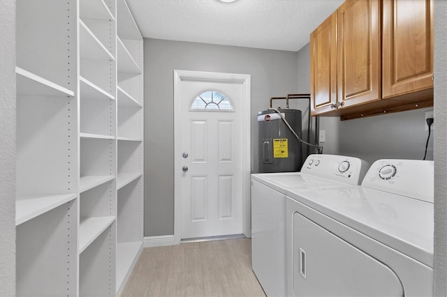 laundry area featuring cabinets, a textured ceiling, light wood-type flooring, electric water heater, and independent washer and dryer