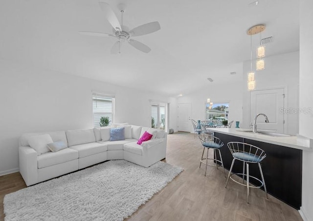 living room featuring light hardwood / wood-style floors, lofted ceiling, sink, and ceiling fan