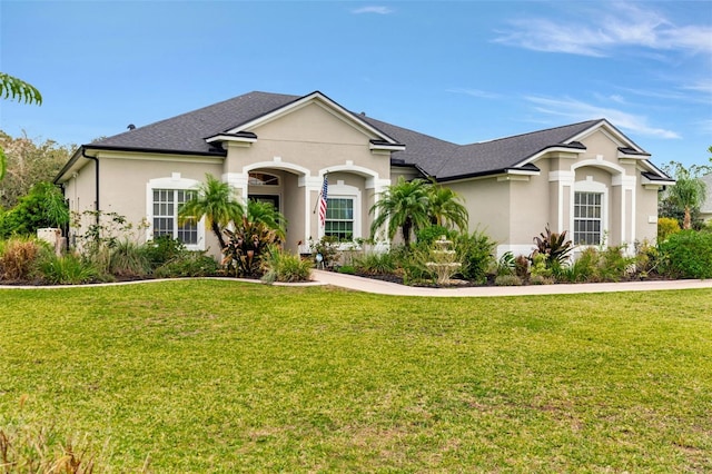 view of front facade with roof with shingles, a front lawn, and stucco siding