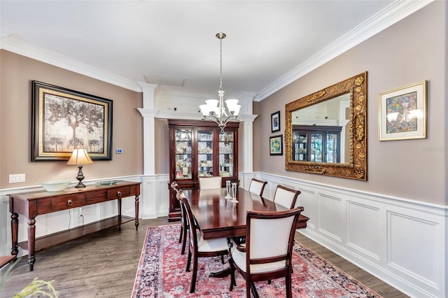 dining room with wood finished floors, ornamental molding, wainscoting, decorative columns, and an inviting chandelier