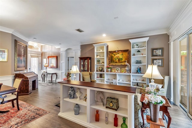 interior space featuring wainscoting, crown molding, ornate columns, and wood finished floors