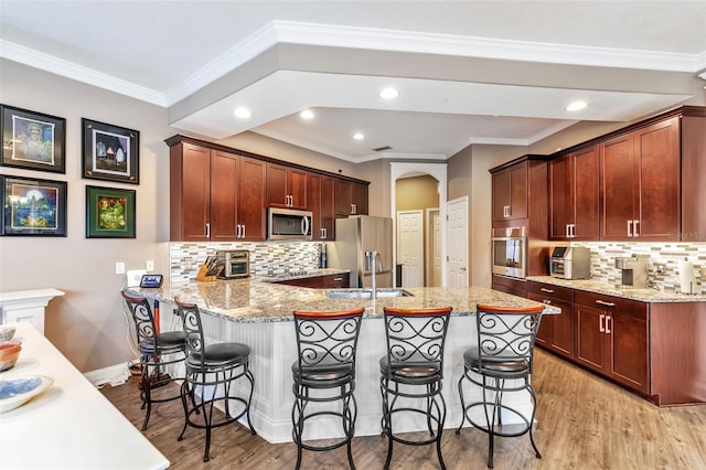 kitchen with arched walkways, appliances with stainless steel finishes, a peninsula, light wood-style floors, and a kitchen bar