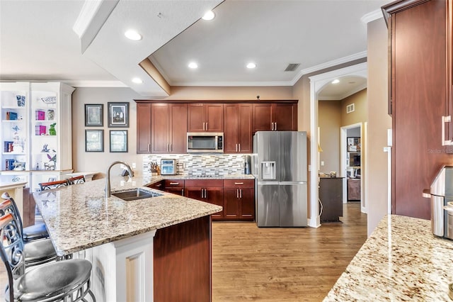 kitchen with stainless steel appliances, a sink, visible vents, light stone countertops, and a kitchen bar