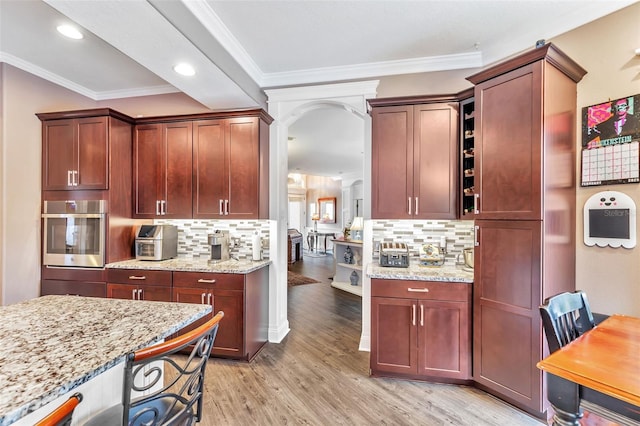 kitchen featuring arched walkways, ornamental molding, light stone countertops, light wood-style floors, and stainless steel oven