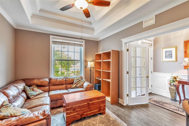 living area featuring wood finished floors, visible vents, ornamental molding, wainscoting, and a raised ceiling