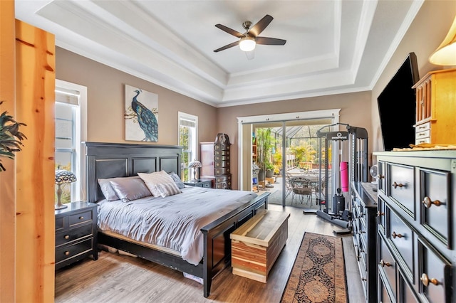 bedroom featuring light wood-style floors, access to outside, a tray ceiling, and crown molding