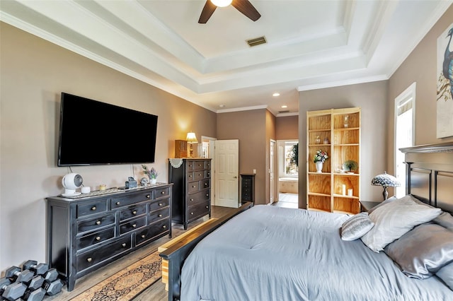 bedroom featuring visible vents, a raised ceiling, ornamental molding, wood finished floors, and ensuite bathroom