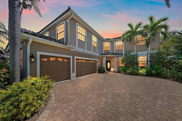 view of front of home featuring a garage, a tile roof, decorative driveway, and stucco siding