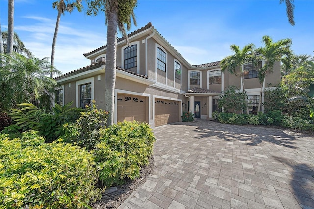 view of front of house with a garage, decorative driveway, a tile roof, and stucco siding