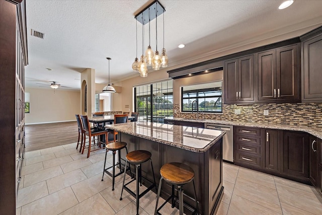 kitchen with dark brown cabinetry, tasteful backsplash, dishwasher, light stone counters, and a center island