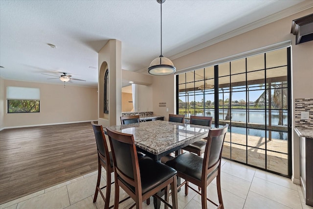 dining area featuring crown molding, a water view, ceiling fan, a textured ceiling, and baseboards