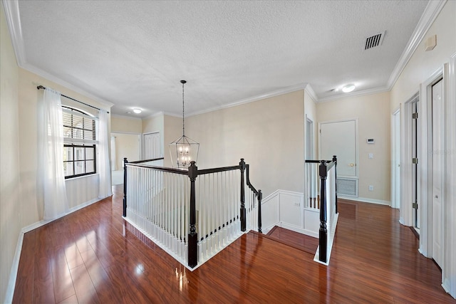 corridor with wood finished floors, visible vents, an upstairs landing, ornamental molding, and an inviting chandelier