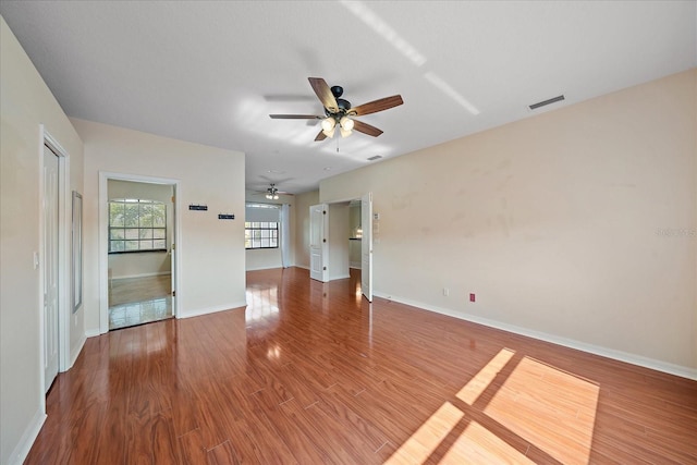 unfurnished living room with a ceiling fan, visible vents, baseboards, and wood finished floors