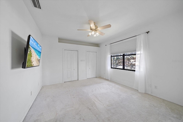 unfurnished bedroom featuring carpet flooring, two closets, visible vents, and a ceiling fan