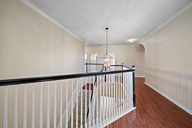 hall with arched walkways, wood finished floors, baseboards, ornamental molding, and an inviting chandelier