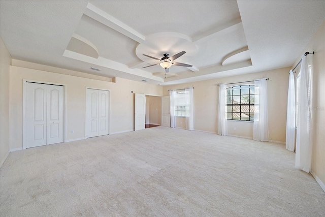 unfurnished bedroom with a tray ceiling, carpet, two closets, and baseboards