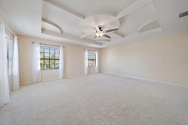 empty room with ceiling fan, visible vents, a raised ceiling, and a textured ceiling