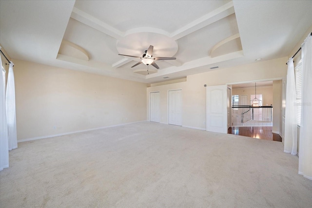 unfurnished bedroom featuring carpet floors, a tray ceiling, baseboards, and ceiling fan with notable chandelier