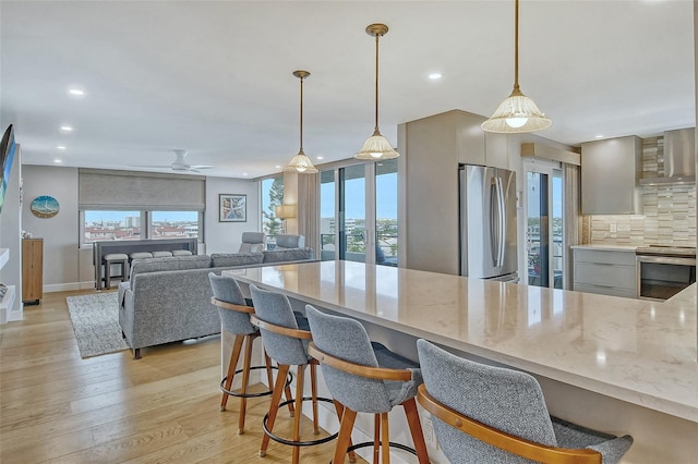 kitchen with backsplash, wall chimney range hood, a wealth of natural light, light wood-style flooring, and appliances with stainless steel finishes