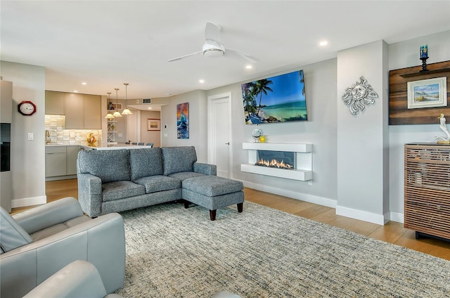 living area with baseboards, recessed lighting, light wood-style flooring, a glass covered fireplace, and a ceiling fan