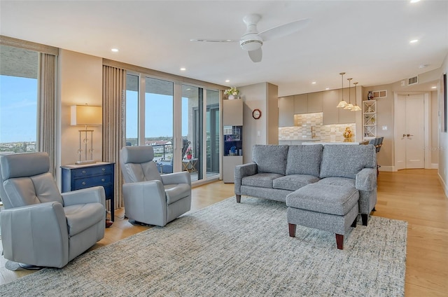 living area with light wood-type flooring, visible vents, recessed lighting, a wall of windows, and ceiling fan