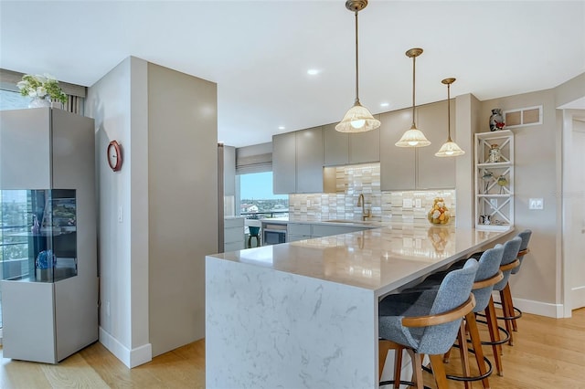 kitchen featuring tasteful backsplash, light wood finished floors, a kitchen bar, a peninsula, and a sink