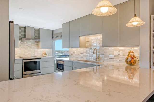 kitchen with gray cabinets, a sink, stainless steel appliances, wall chimney range hood, and backsplash