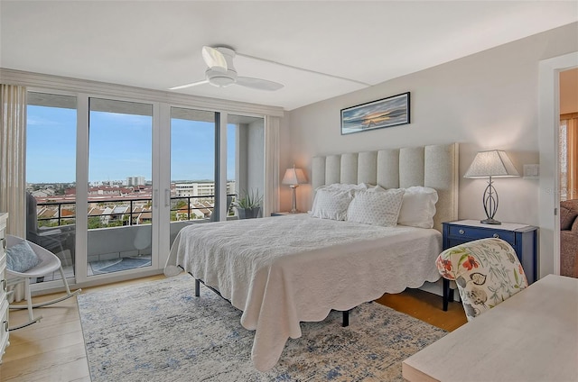 bedroom featuring access to exterior, ceiling fan, expansive windows, light wood-style floors, and a view of city