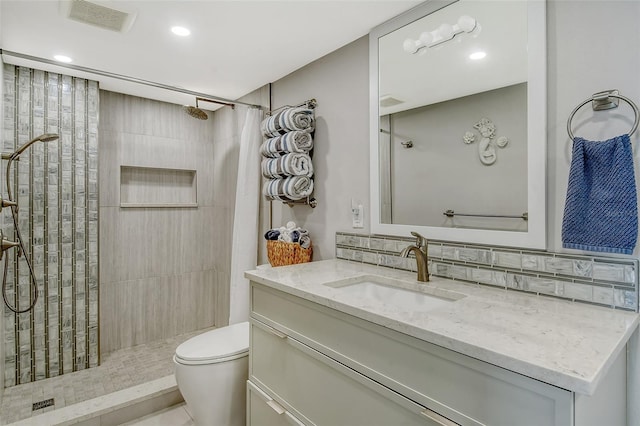 bathroom with visible vents, toilet, tasteful backsplash, a tile shower, and vanity