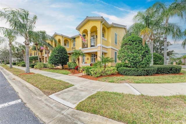 mediterranean / spanish-style house with a balcony, a front yard, and stucco siding