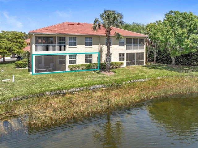 rear view of house with a water view, a sunroom, a tile roof, and a lawn