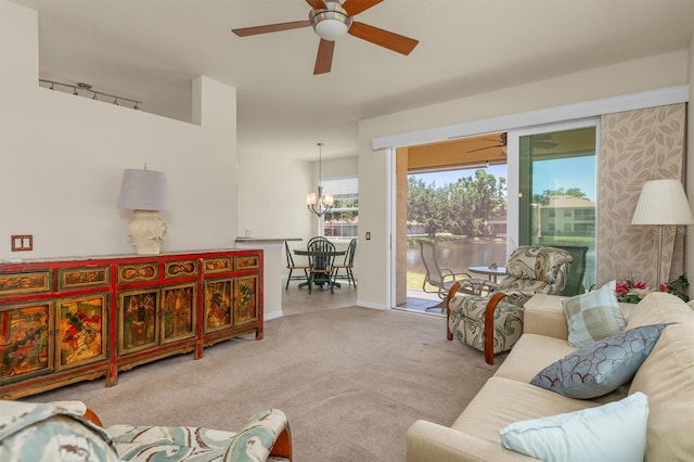 living room featuring light carpet, ceiling fan with notable chandelier, a water view, and baseboards