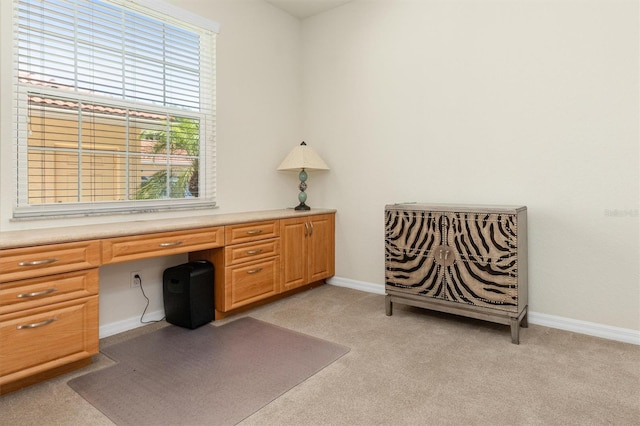 home office with light colored carpet, built in study area, and baseboards