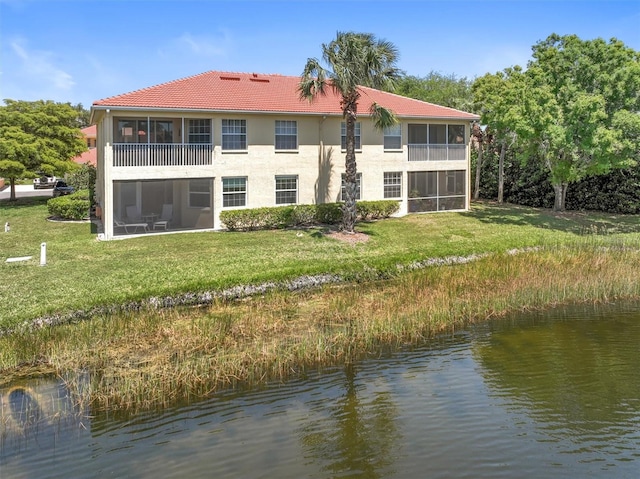 back of house featuring a tile roof, a sunroom, a water view, and a yard