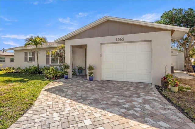 ranch-style home with a garage, central AC unit, decorative driveway, a front lawn, and stucco siding