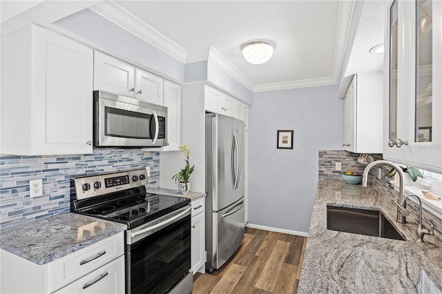 kitchen featuring appliances with stainless steel finishes, glass insert cabinets, white cabinetry, a sink, and light stone countertops