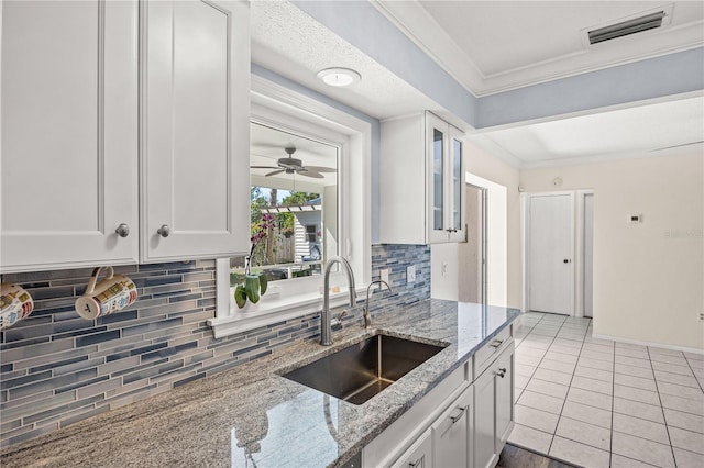 kitchen with visible vents, glass insert cabinets, white cabinetry, a sink, and light stone countertops