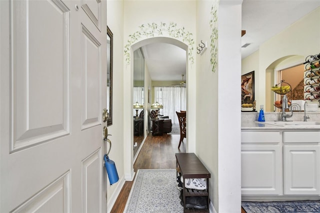 foyer entrance featuring arched walkways, visible vents, a ceiling fan, baseboards, and dark wood-style floors