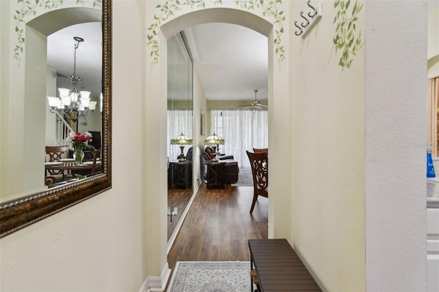 hallway with an inviting chandelier, arched walkways, and dark wood finished floors