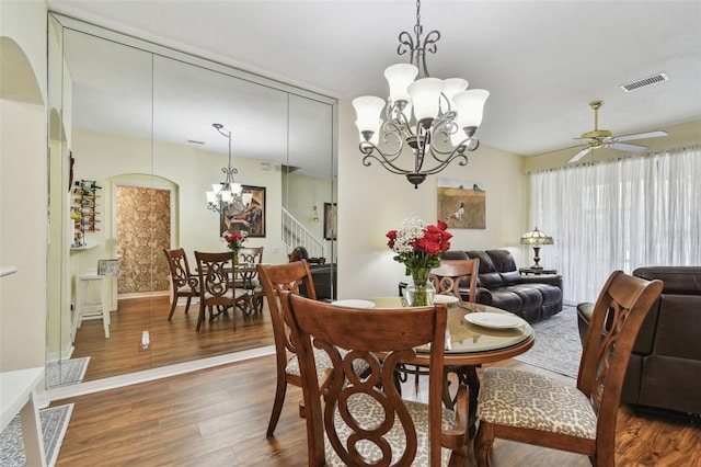 dining space featuring stairway, visible vents, dark wood-style flooring, and ceiling fan with notable chandelier