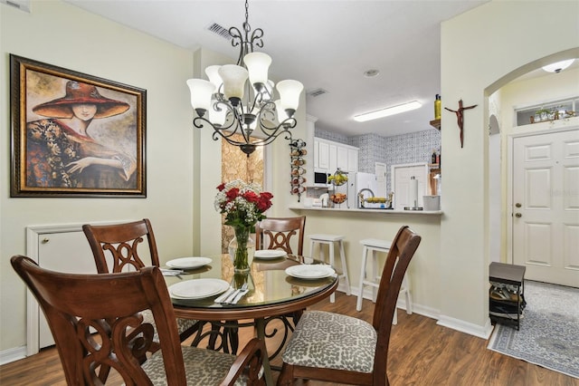 dining room featuring a notable chandelier, baseboards, arched walkways, and dark wood-style flooring