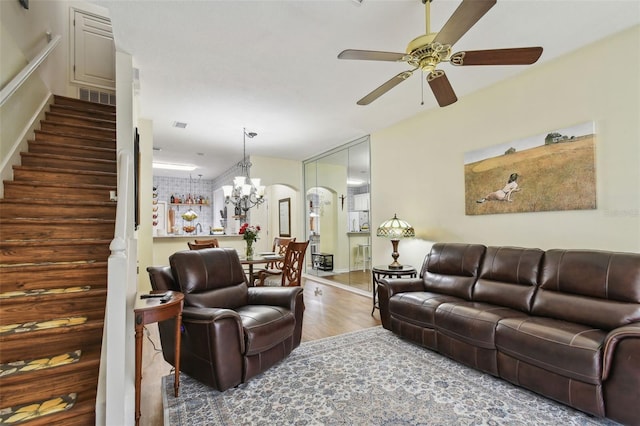 living area featuring stairway, visible vents, wood finished floors, and ceiling fan with notable chandelier