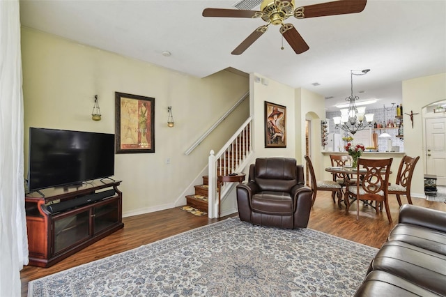 living area with arched walkways, ceiling fan with notable chandelier, dark wood-type flooring, baseboards, and stairway