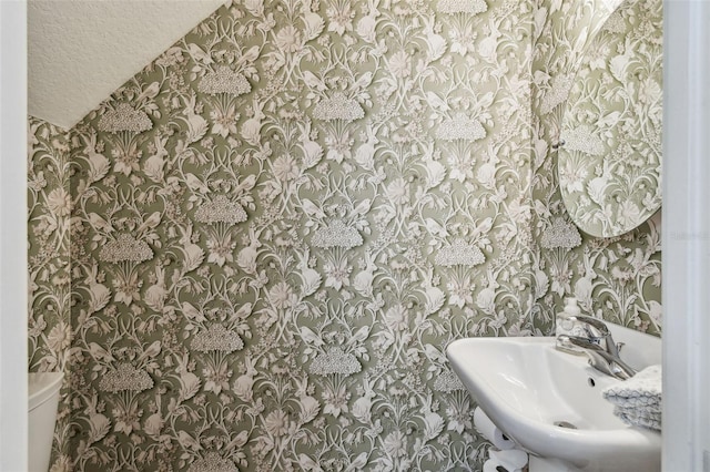 half bathroom with a sink, toilet, and wallpapered walls