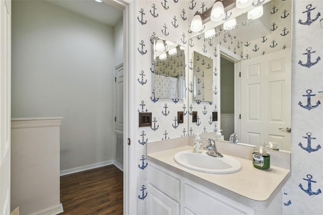 bathroom with baseboards, wood finished floors, vanity, and wallpapered walls