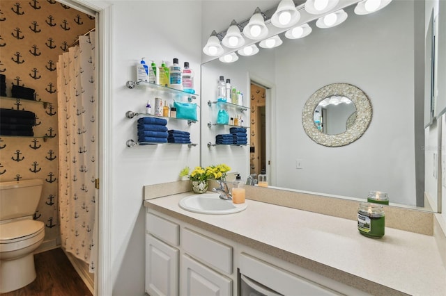 bathroom with toilet, wallpapered walls, wood finished floors, and vanity